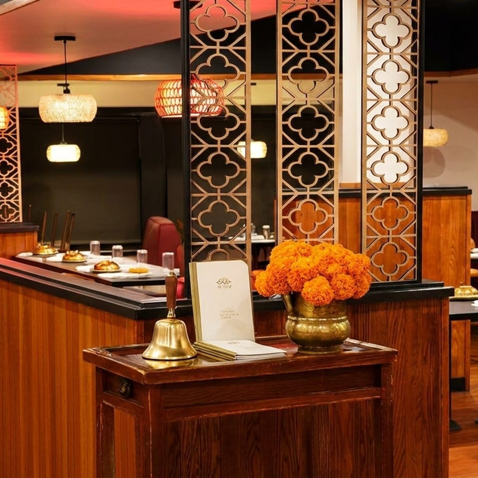 Elegant restaurant interior with red booths, patterned screens, warm pendant lighting, polished wood, and a flower-adorned host stand.