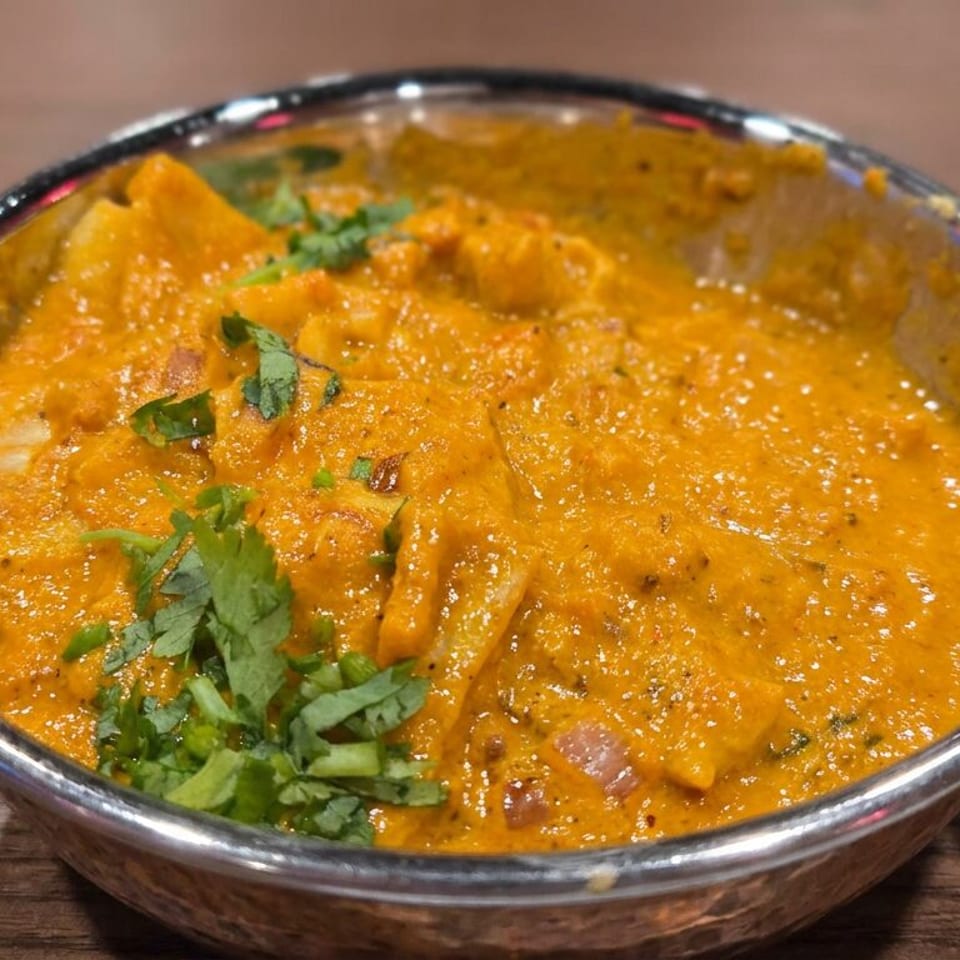 Creamy orange curry garnished with fresh cilantro, served in an ornate handled metal bowl on a wooden table.